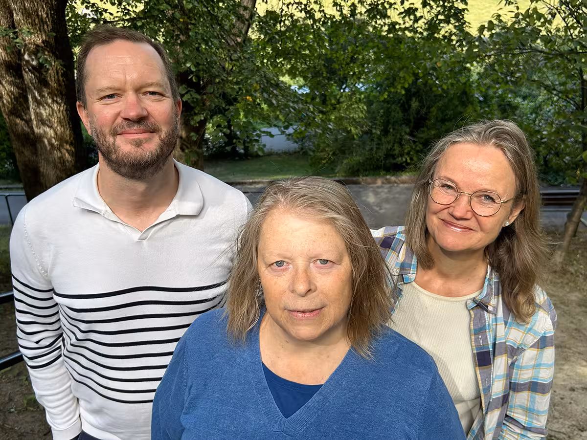 Mann og to kvinner står i trapp ute og ser inn i kamera. 