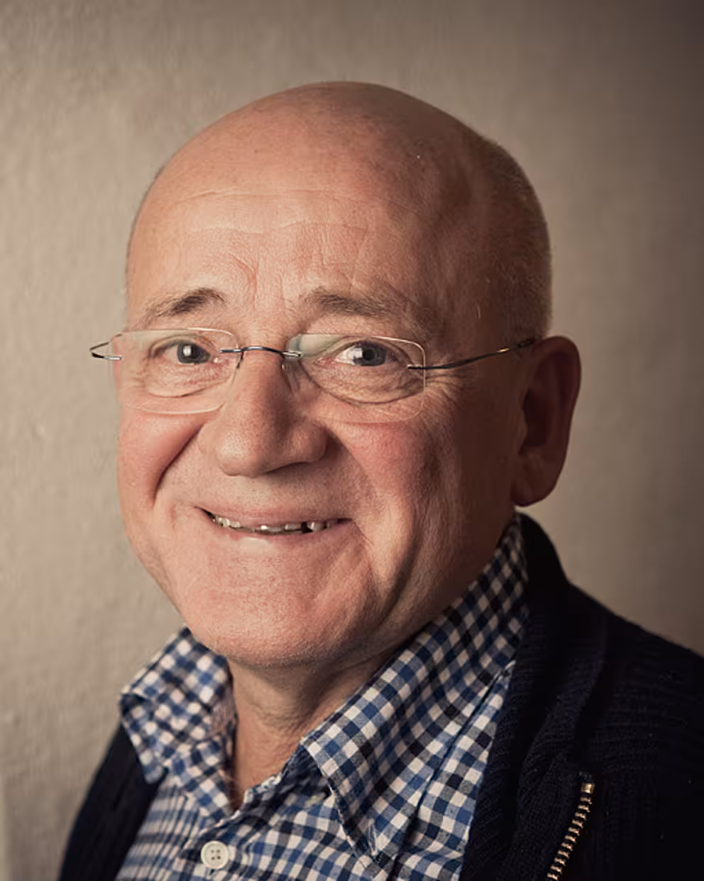 Eldre, smilende mann med briller, ikledd rutete skjorte og genser