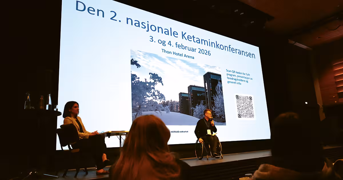 Bilde av mann i rullestol og en kvinne i en stol på en scene foran et bilde