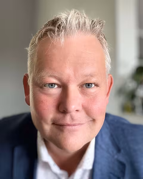 Smilende mann med lyseblondt hår i dressjakke og hvit skjorte