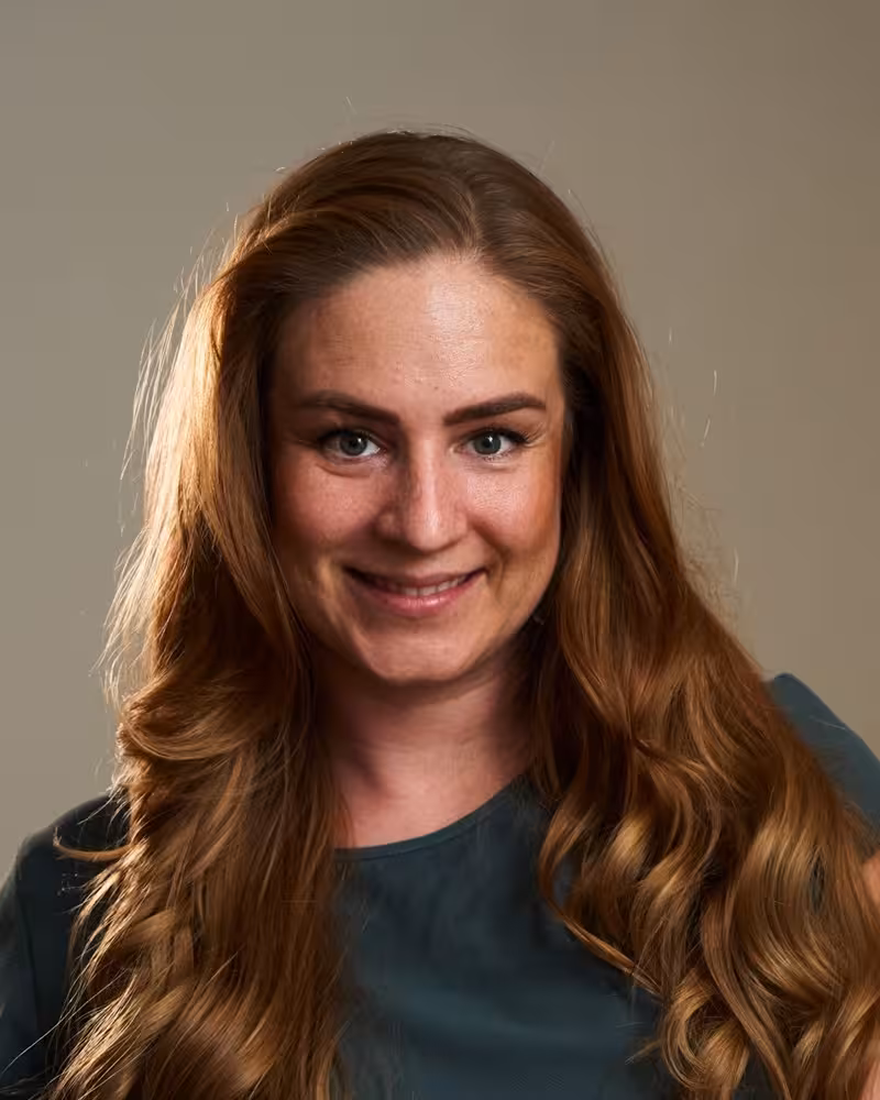 Sittende, smilende kvinne mot en beige bakgrunn