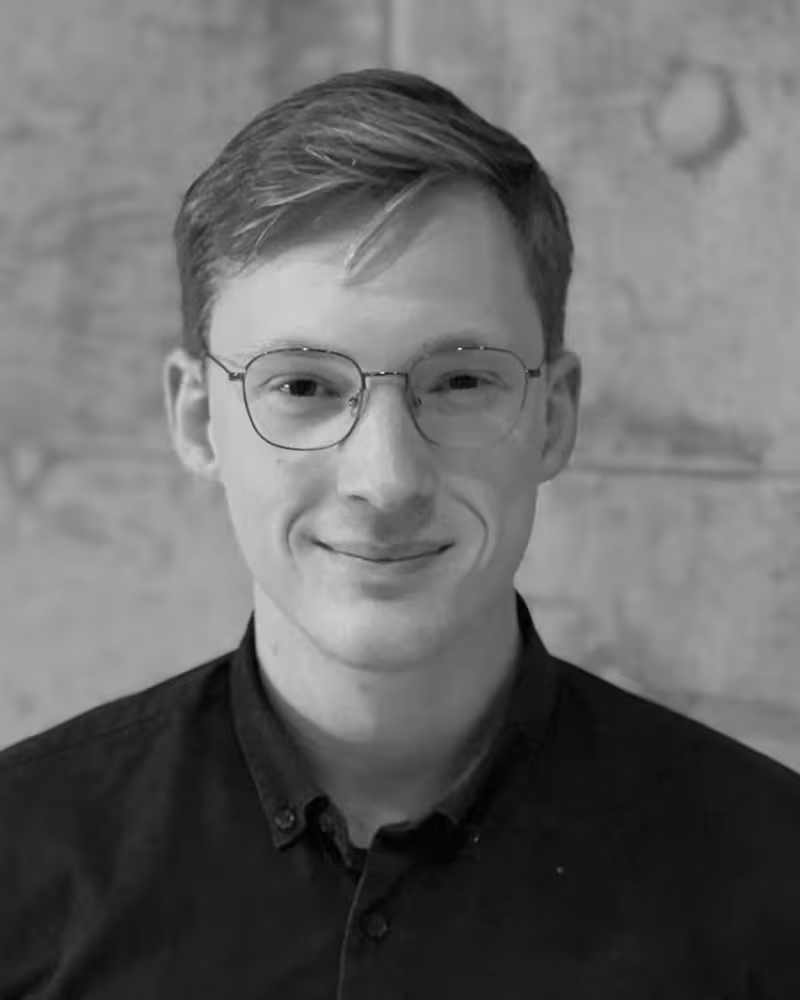 Svart-hvitt bilde av en ung, smilende mann med lyst hår og briller