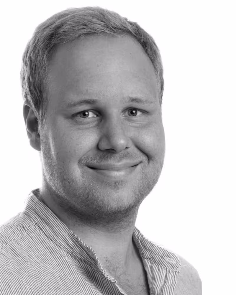 Svart-hvitt bilde av en ung, smilende mann med lyst hår og briller