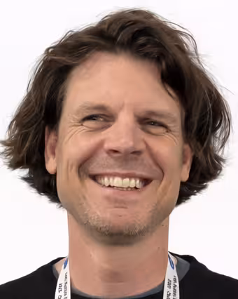 Smilende mann med mørkt hår og sort genser.